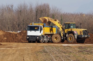 A large bulldozer spills earth and stone in the trailer of an heavy dumper truck at the just opened...
