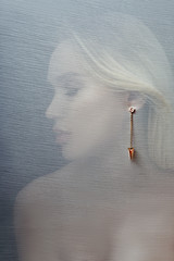 Earrings and jewelry in the ear of a sexy woman inserted through a transparent fabric. Perfect blonde girl, gorgeous mysterious look. Advertising jewelry, beautiful earrings in the girl ear