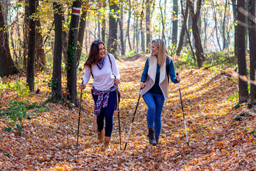 Two young girls walking in forest with backpacks using sticks with fall leaves and trees on background