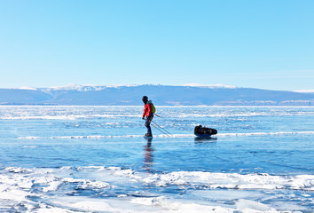 A tourist on skates with a tent, in a protective helmet and a red jacket travels on the ice of frozen Baikal lake along Olkhon Island