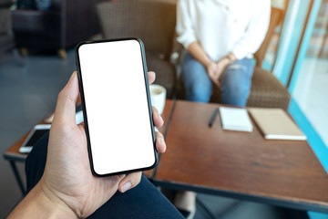 Mockup image of a man's hand holding black mobile phone with blank white screen with woman sitting in cafe