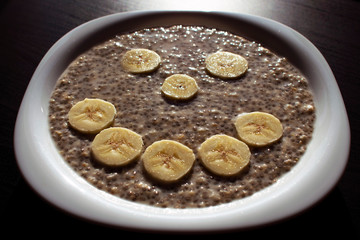 Chia seeds and oat flakes in water, with banana slices arranged in smiley face on a white plate. Perfect breakfast.