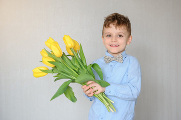 close up photo of a little boy with yellow tulips in his hands indoors