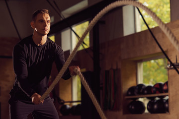 Fit, sporty and athletic sportsman working in a gym. Man training using battle ropes. Sports, athletics and fitness concept.