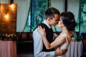 A beautiful young couple performs their first wedding dance. The bride in a chic white dress and her groom are in the center of the wedding hall