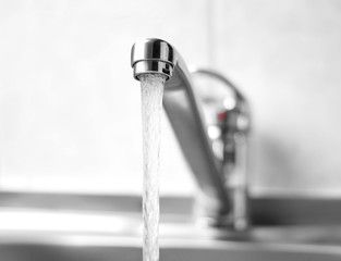 Water runs from a metal water tap. Close up
