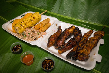 Fiesta plate with Chamorro finadene sauce. Guam local food. Banana leaves background. Bbq ribs, bbq-chicken, kelaguen, red-rice, corn on the cob, fried-lumpia