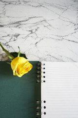Yellow rose flower and blank, open notebook on top of marble background. Copy space with lined paper.