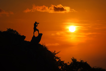 Silhouette of photographer on top of mountain at sunset red sky