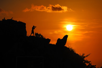 Silhouette of photographer on top of mountain at sunset red sky