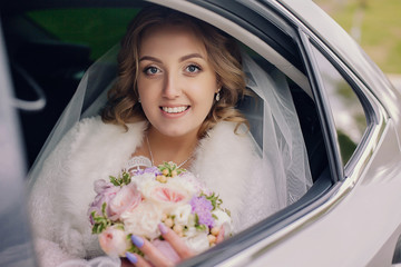 Young bride in a wedding car. Bridal bouquet.