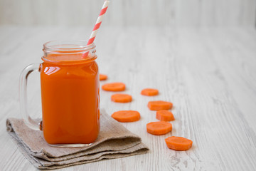 Glass jar of carrot smoothie on white wooden surface, side view. Copy space.
