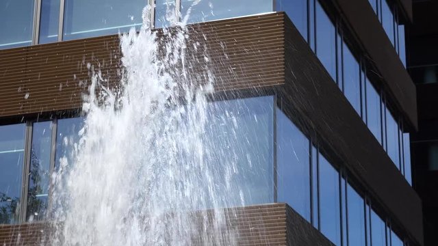 A windowed office building - closeup - a water from a fountain gushes in the foreground