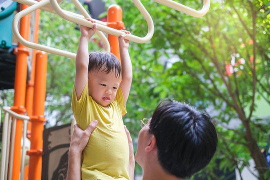 Father And Cute Little Asian 2 - 3 Years Old Toddler Baby Boy Child Having Fun Exercising Outdoor And Dad Help Catch Up On Monkey Bars Equipment At Playground On Nature At Park, Father's Day Concept