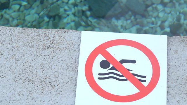 Closeup on a no swimming sign by a decorative fountain pool