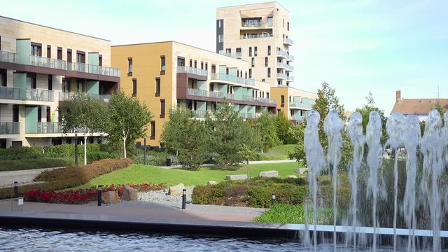 A beautiful apartment building complex with a small park on a sunny day - a water fountain in the foreground