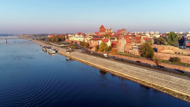 Torun old city in Poland. Aerial flyby video in sunrise light with medieval Gothic St John Cathedral, town hall tower, historic buildings, town walls, gates and Vistula river with a rowing boat