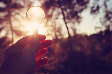 A male hand holds a magnifying glass against the setting sun outside. concept of search, creative...