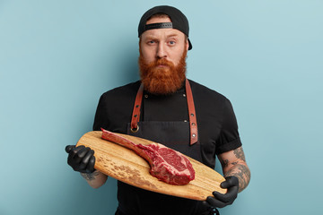 Horizontal shot of self confident satisfied bearded young male cook looks with serious expression,...