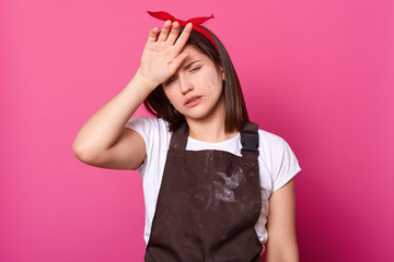 Portrait of girl in brown apron, white t shirt, red hair band, with tired expression on isolated...