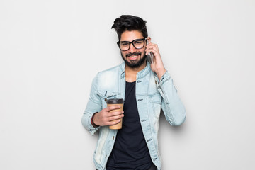 Young handsome Indian man talking on mobile phone holding take away coffee cup isolated on white background
