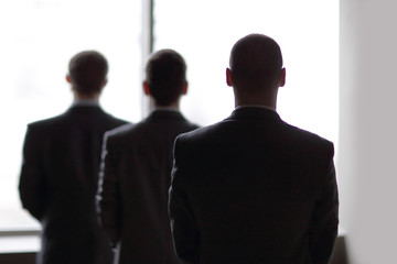 Fototapeta premium rear view of three businessmen as they stare at the big window overlooking the city