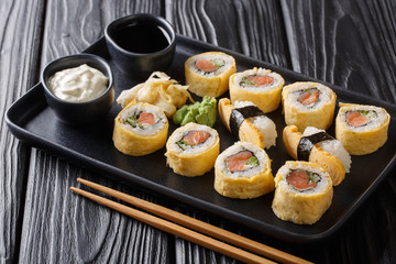 Tamagoyaki omelette set sushi rolls with rice, smoked salmon and avocado close-up with sauces, wasabi and ginger on a black table. horizontal