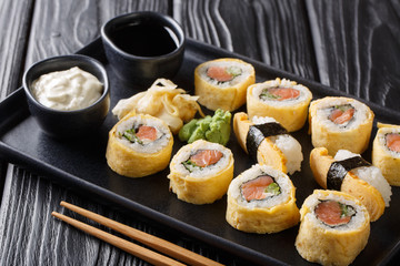Delicious breakfast Tamagoyaki set sushi roll with rice, omelette, cheese, salmon and avocado close-up with sauces, wasabi and ginger. horizontal