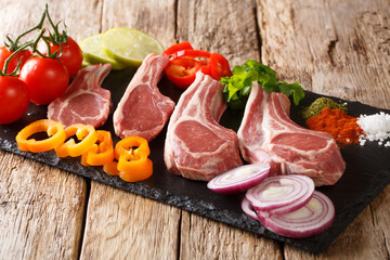 Preparation for grilling raw Lamb chops with fresh vegetables and spices close-up on a slate board. horizontal