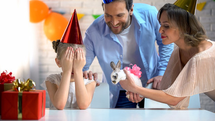 Parents presenting cute bunny for daughter, girl with eyes closed, b-day party