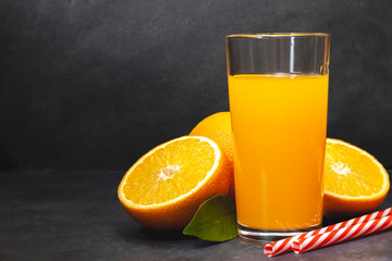 Gass of fresh orange juice with fresh fruits on dark table