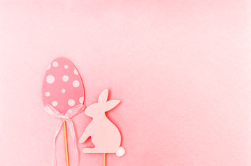 Easter composition with traditional decor. Wooden decorative egg and rabbit figures on soft light pink background.
