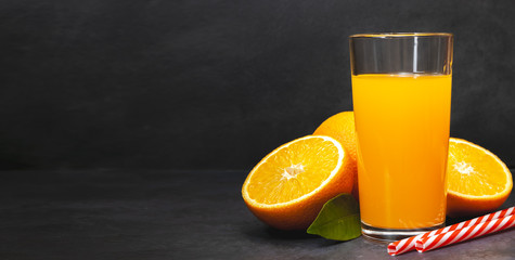 Gass of fresh orange juice with fresh fruits on dark table