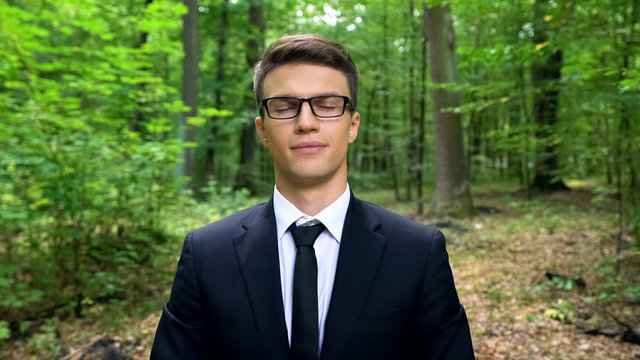 Business person with closed eyes breathing deeply in forest, air freshener