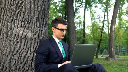 Inspired young businessman working on grass in park, escaping office routine