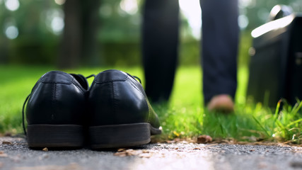 Black shoes standing on grass, businessman walking barefoot in park copes stress