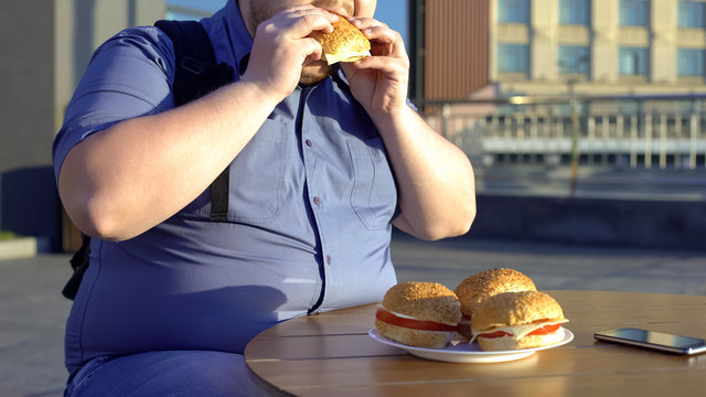 Obese bachelor eating fast food hamburger, unhealthy lifestyle, overweight