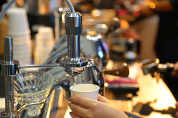 Barista preparing long black or Americano coffee with espresso machine in morning with warm light