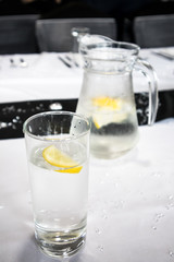 Clear glass with water, ice and lemon slices on white background with glitter on table laid out for a party meal