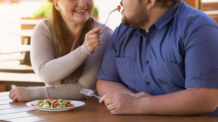 Pretty smiling woman feeding boyfriend with vegetable salad, healthy food, diet