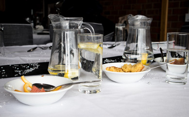 Table with remenants of a celebration meal with dessert bowls with food, glasses and jugs of water