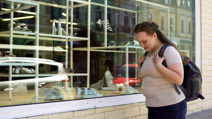 Upset overweight female crying in front of expensive shoes boutique poor student