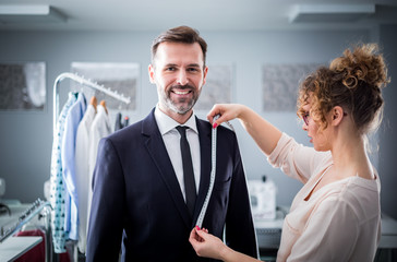 Tailor using tape to measuring smiling client for sewing suit at atelier