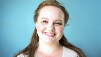 Beautiful caucasian woman smiling at camera on blue background, youth happiness