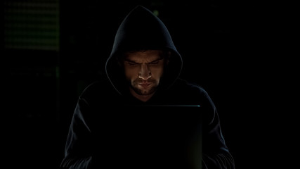 Man in hoodie typing on laptop, cyberbullying or hacking, internet security