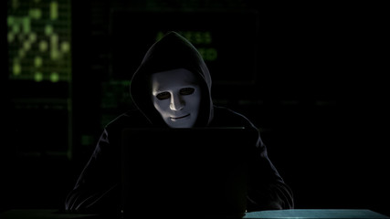 Man in mask cracking codes on laptop, falsification in elections, vote rigging