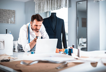 Tailor during work using laptop, modern fashion designer at workshop