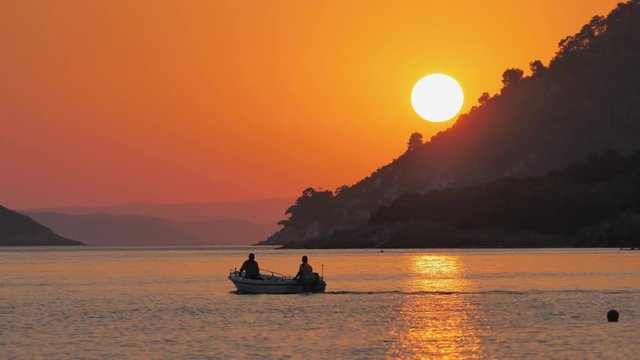 Isolated motor boat go on peaceful sea water, evening sun lightning over islands