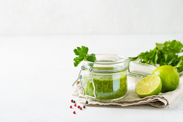 Green sauce chimichurri with fresh herb and spices in jar on white background