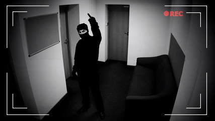 Dangerous criminal in balaclava showing middle finger at surveillance camera